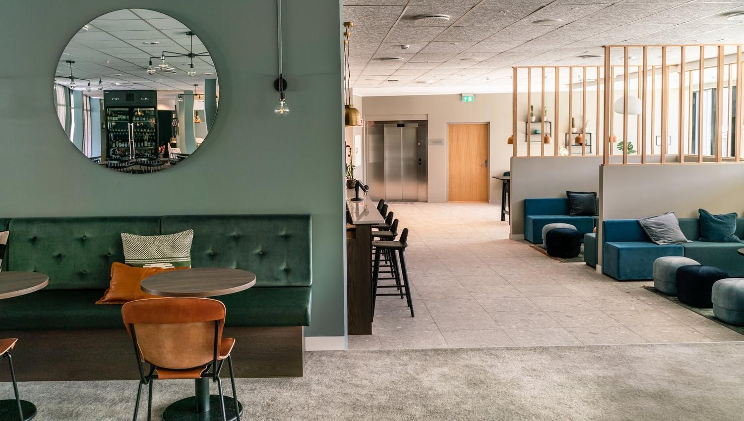 Modern café area with green seating and a round mirror on the wall.