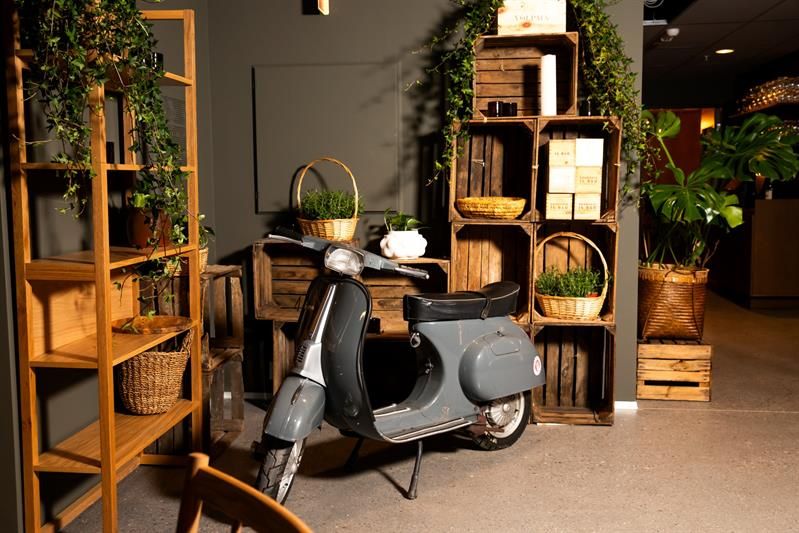 A moped parked inside the venue in front of shelves and baskets filled with plants