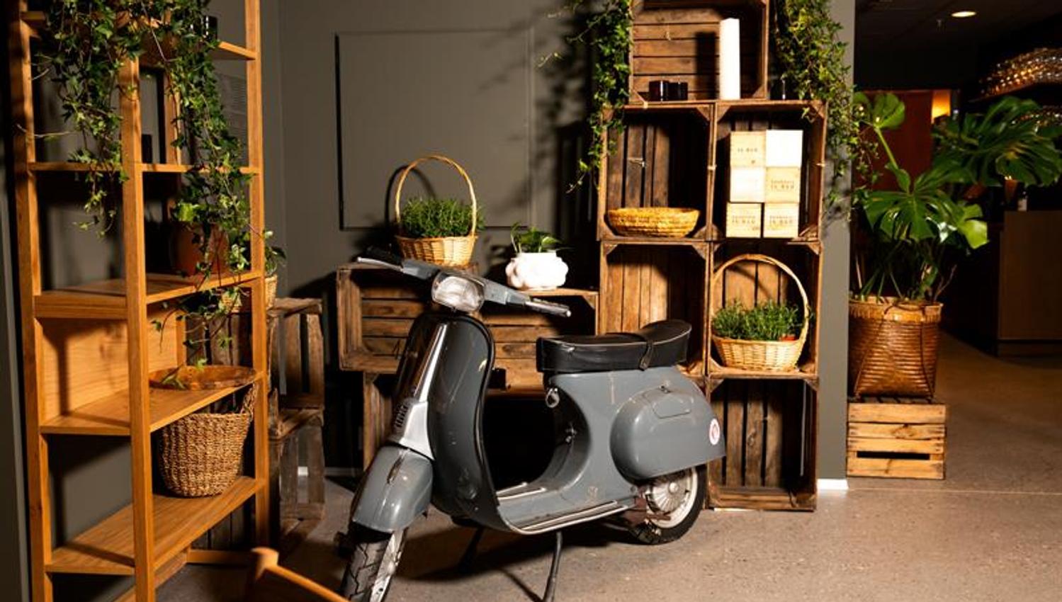 A moped parked inside the venue in front of shelves and baskets filled with plants