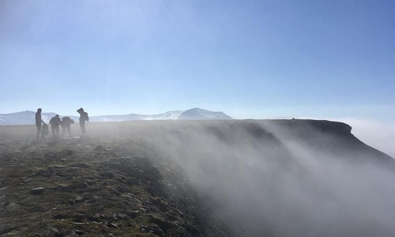 A group of people on top of a mountain with a steep cliff and mist on their right
