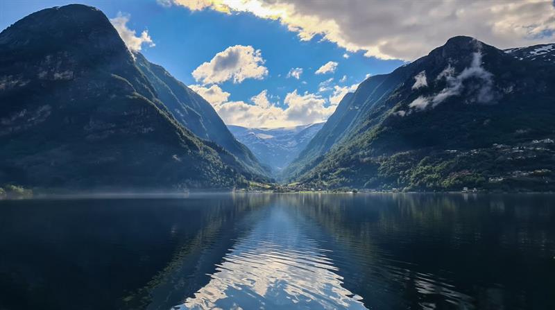 Fjord reflecting mountains and sky in calm water between high peaks.