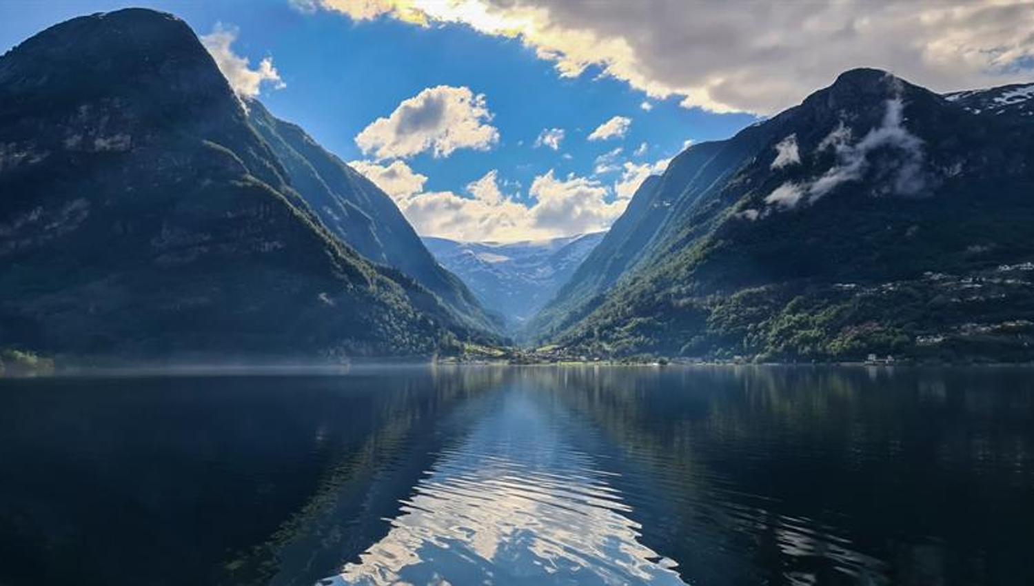 Fjord reflecting mountains and sky in calm water between high peaks.