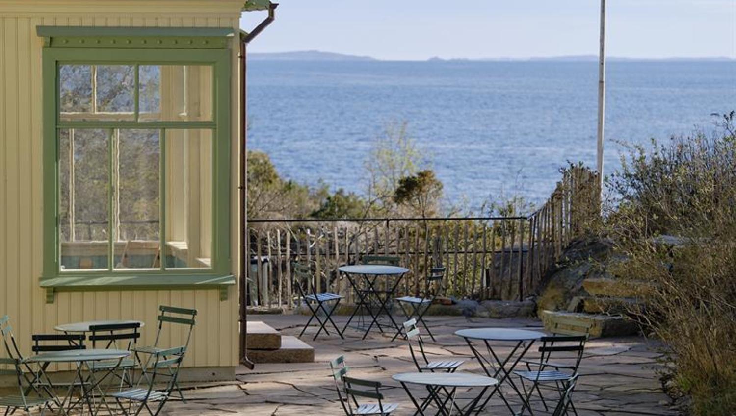 Gult hus med vindu sjøutsikt og terrasse med bord og stoler