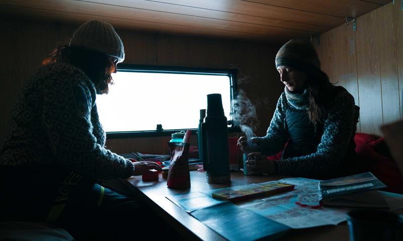 To personer sitter ved et bord inne i en liten villmarkshytte