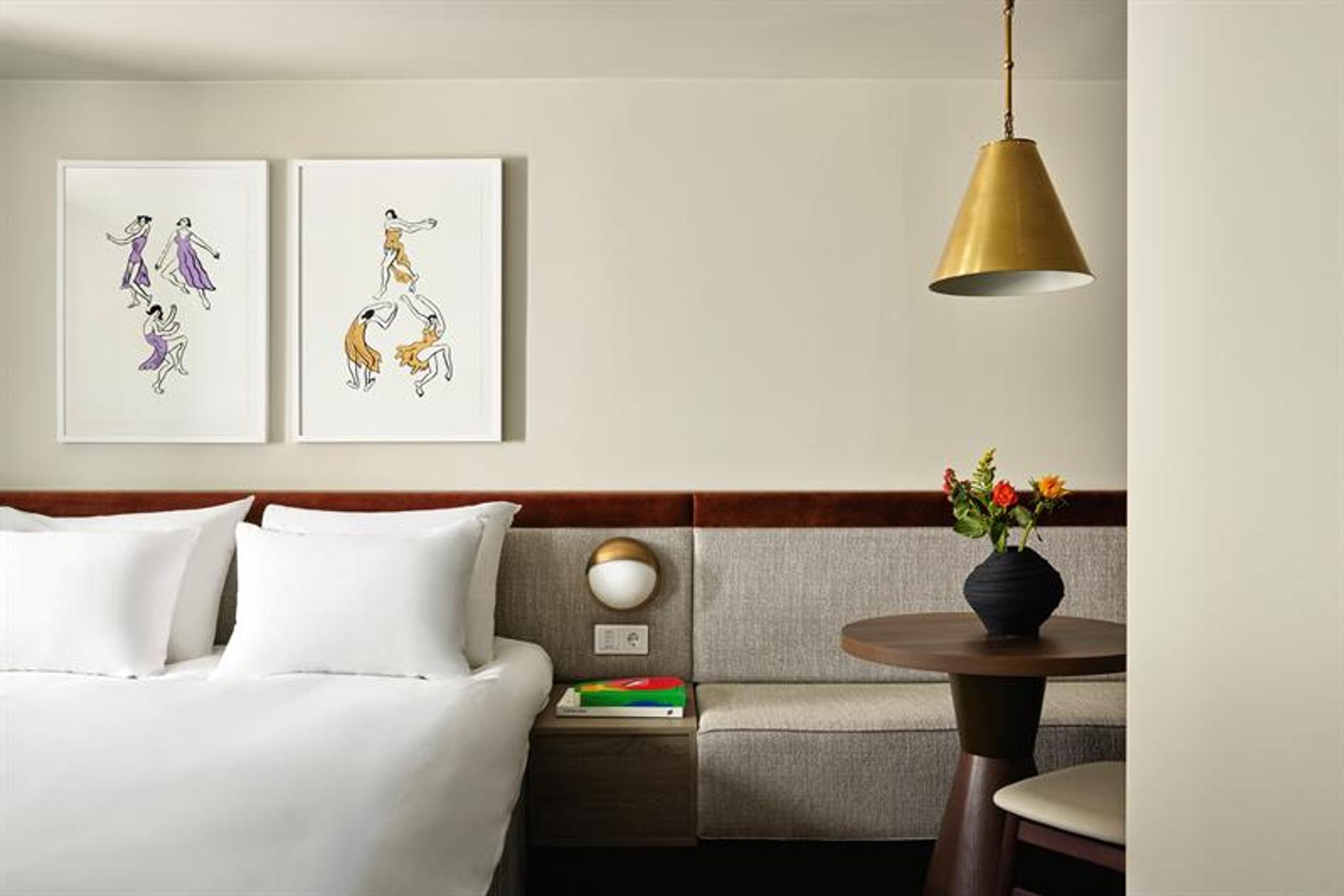 The rooms feature a double bed, integrated seating and wall-mounted lighting. The interior combines textiles, wood finishes and framed artwork.