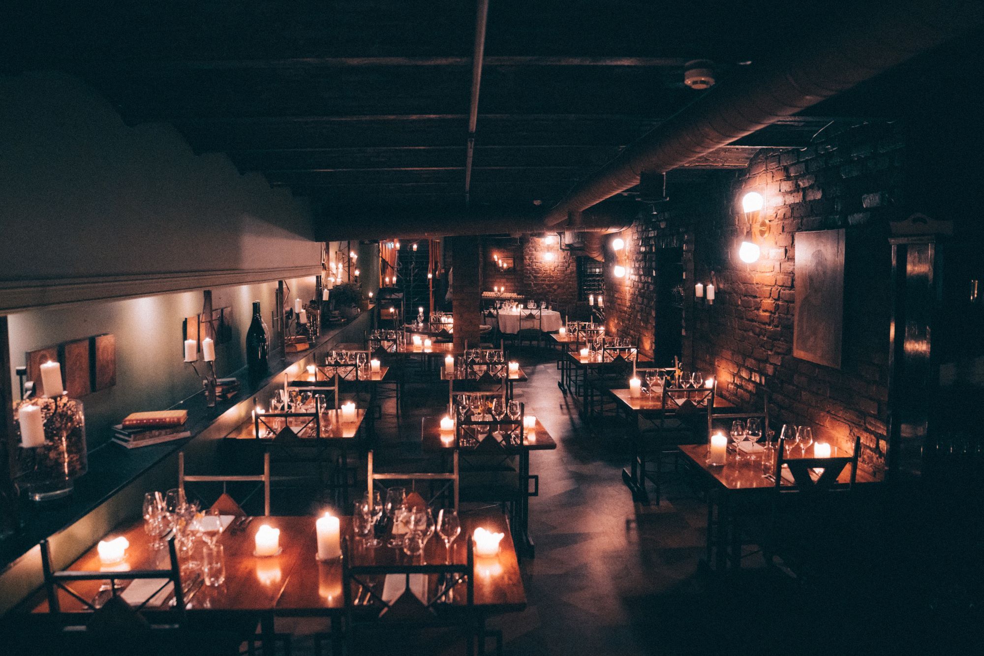 Square dining tables with chairs around them, candlelight, wine glasses, and cutlery on the tables