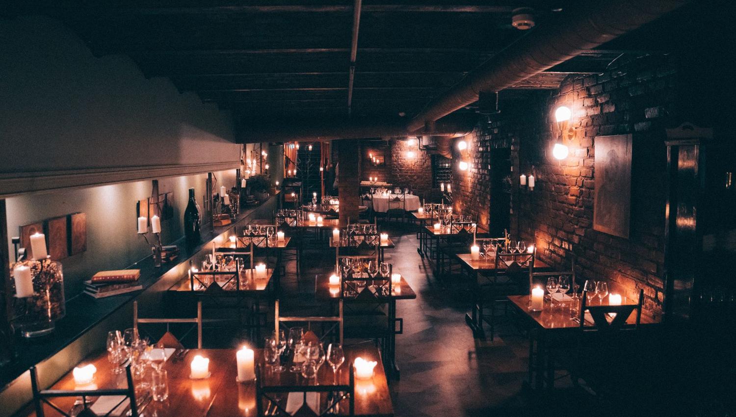 Square dining tables with chairs around them, candlelight, wine glasses, and cutlery on the tables