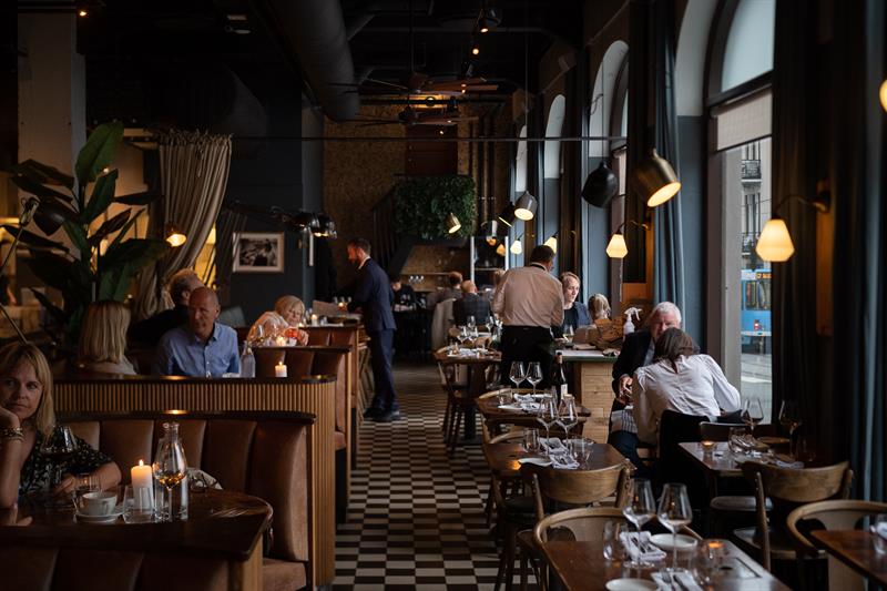 Restaurant interior with large panoramic windows, a chequered floor, and small tables and chairs, with people sitting and eating