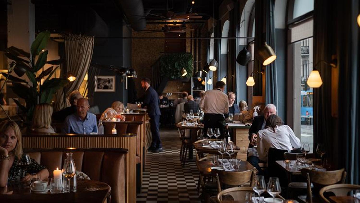 Restaurant interior with large panoramic windows, a chequered floor, and small tables and chairs, with people sitting and eating