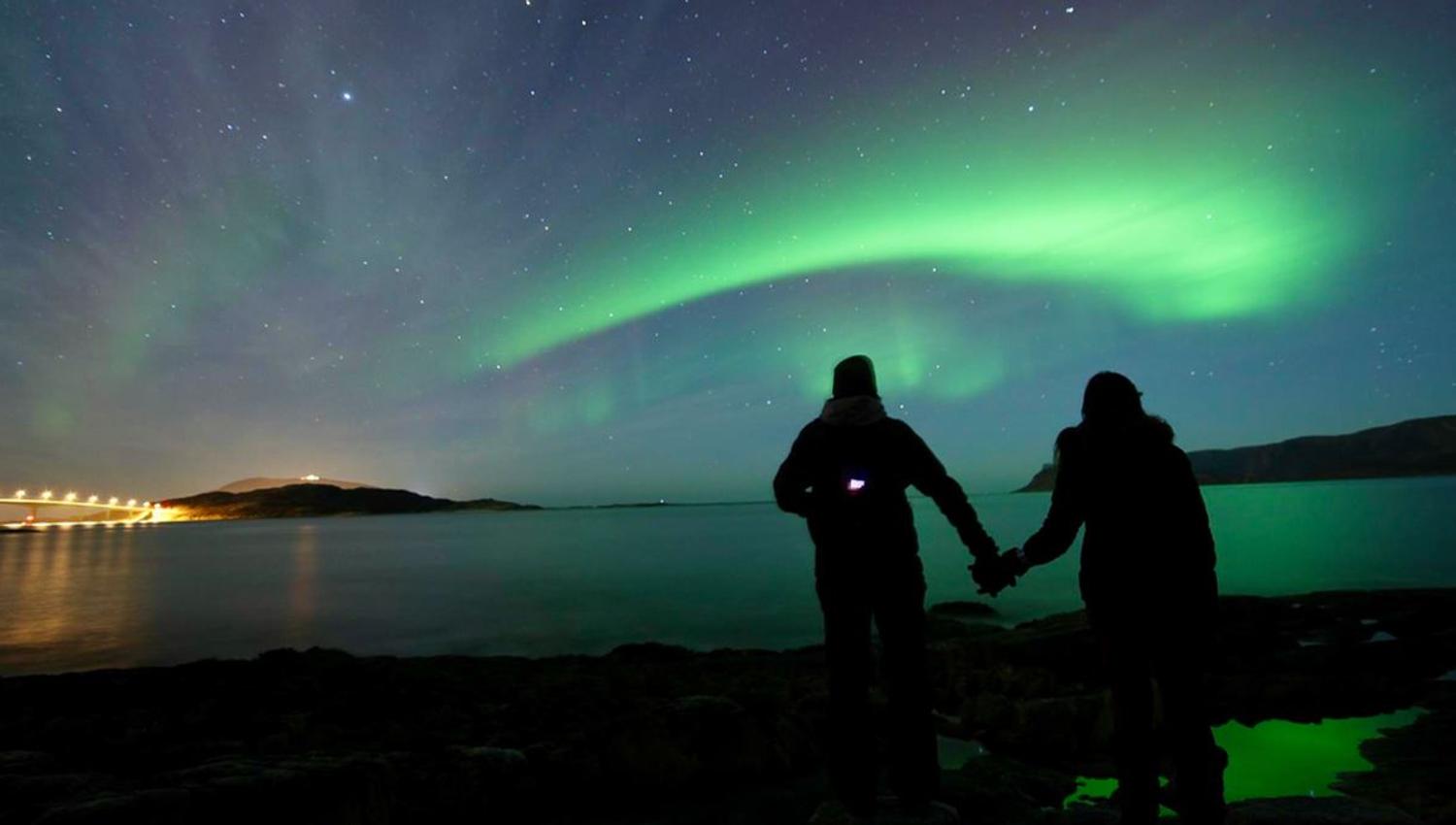 Two guests holding hands under the northern lights