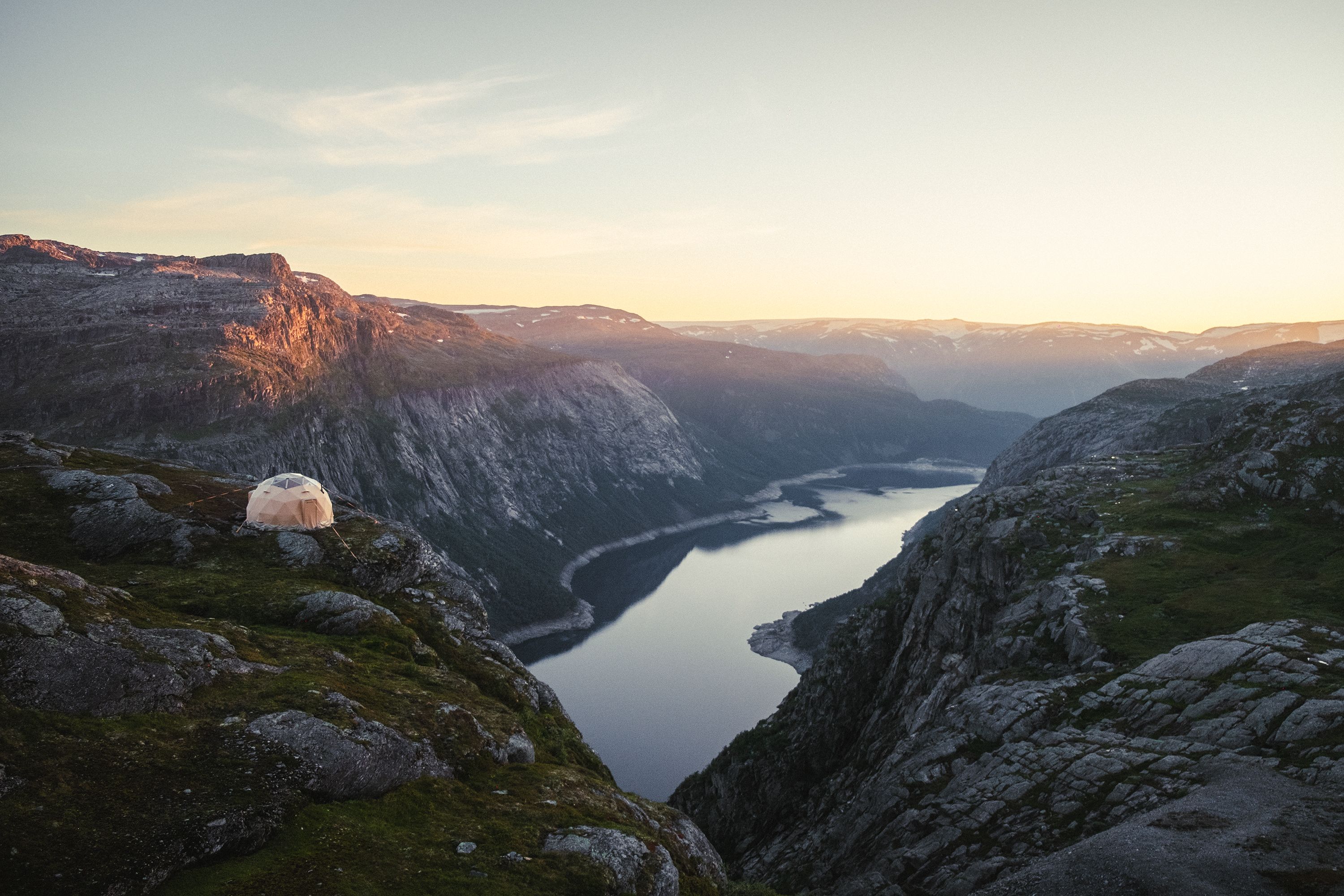 A dome tent on the mountains with views towards a lake. 