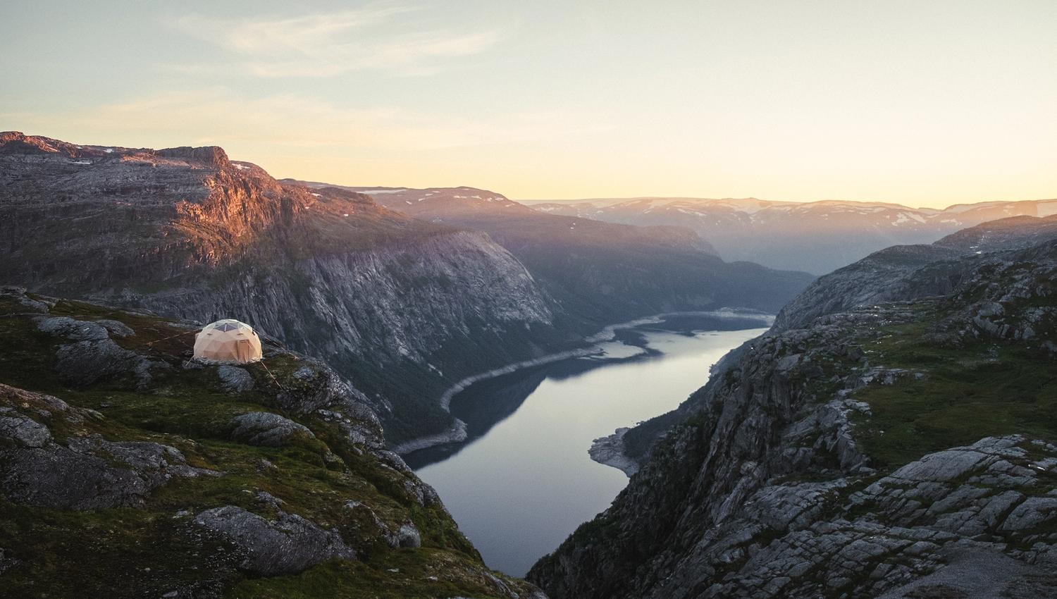 A dome tent on the mountains with views towards a lake.