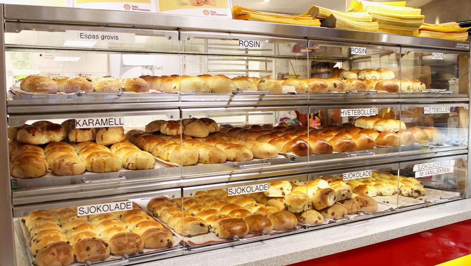 A brightly lit bakery display filled with a wide variety of fresh buns and pastries arranged on multiple shelves.