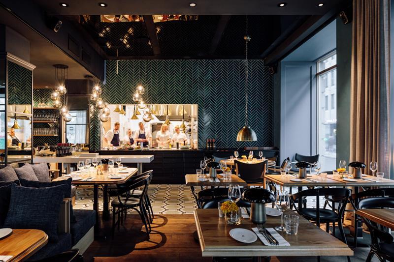 Restaurant Atlas - interior photo. Set tables with chairs, seating section, hanging ceiling lamps and the kitchen in the background.
