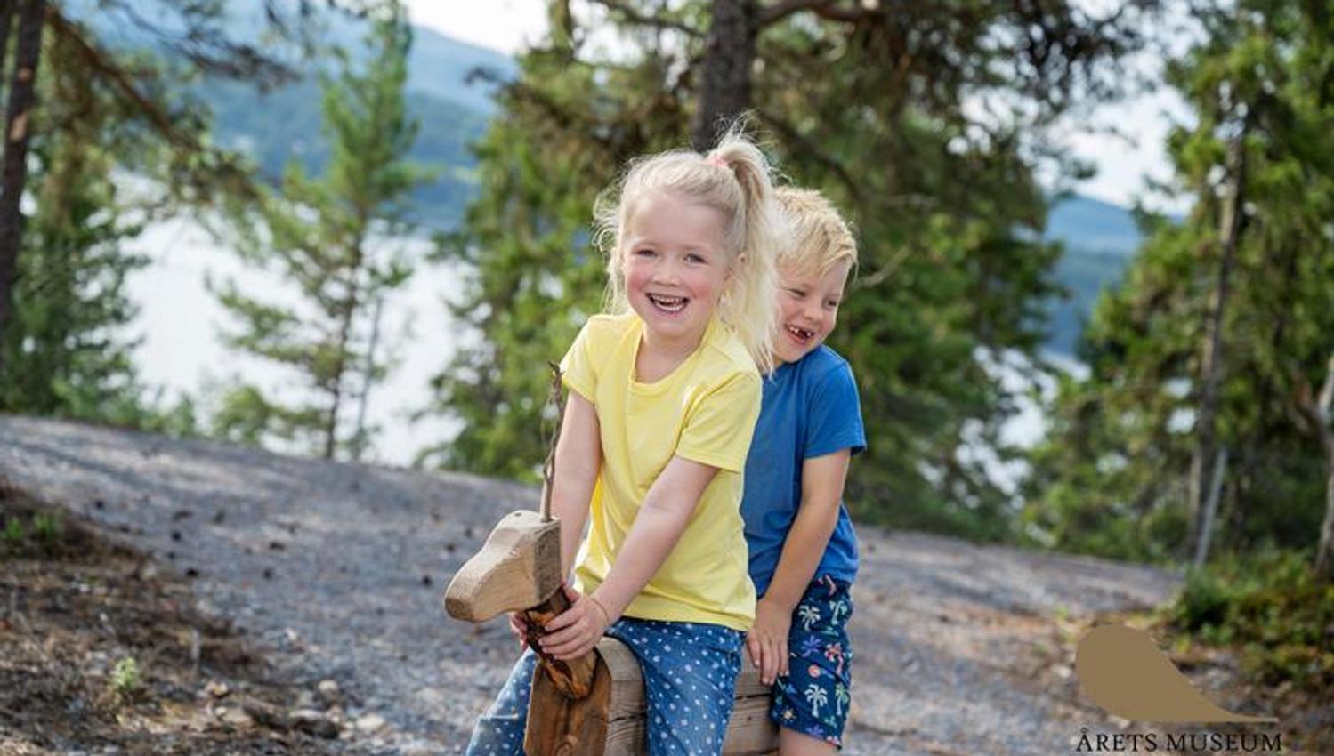 Girl and boy playing on a wooden animal sculpture