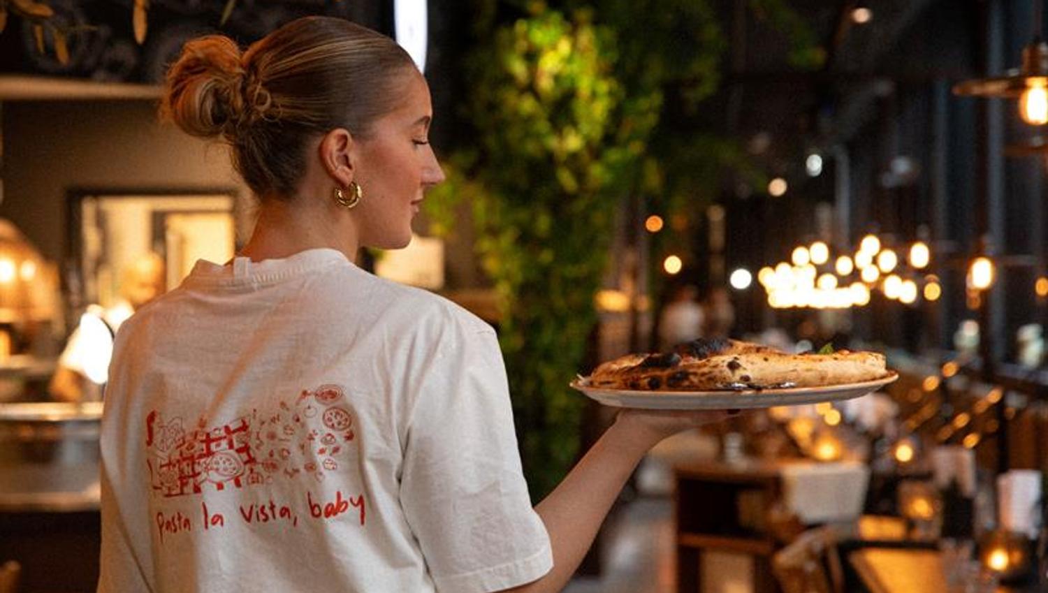 Kvinnelig servitør som bærer en tallerken med pizza
