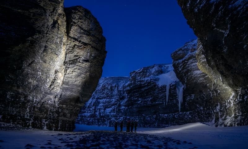 A group of people standing in a valley between mountain cliffs with headplamps on
