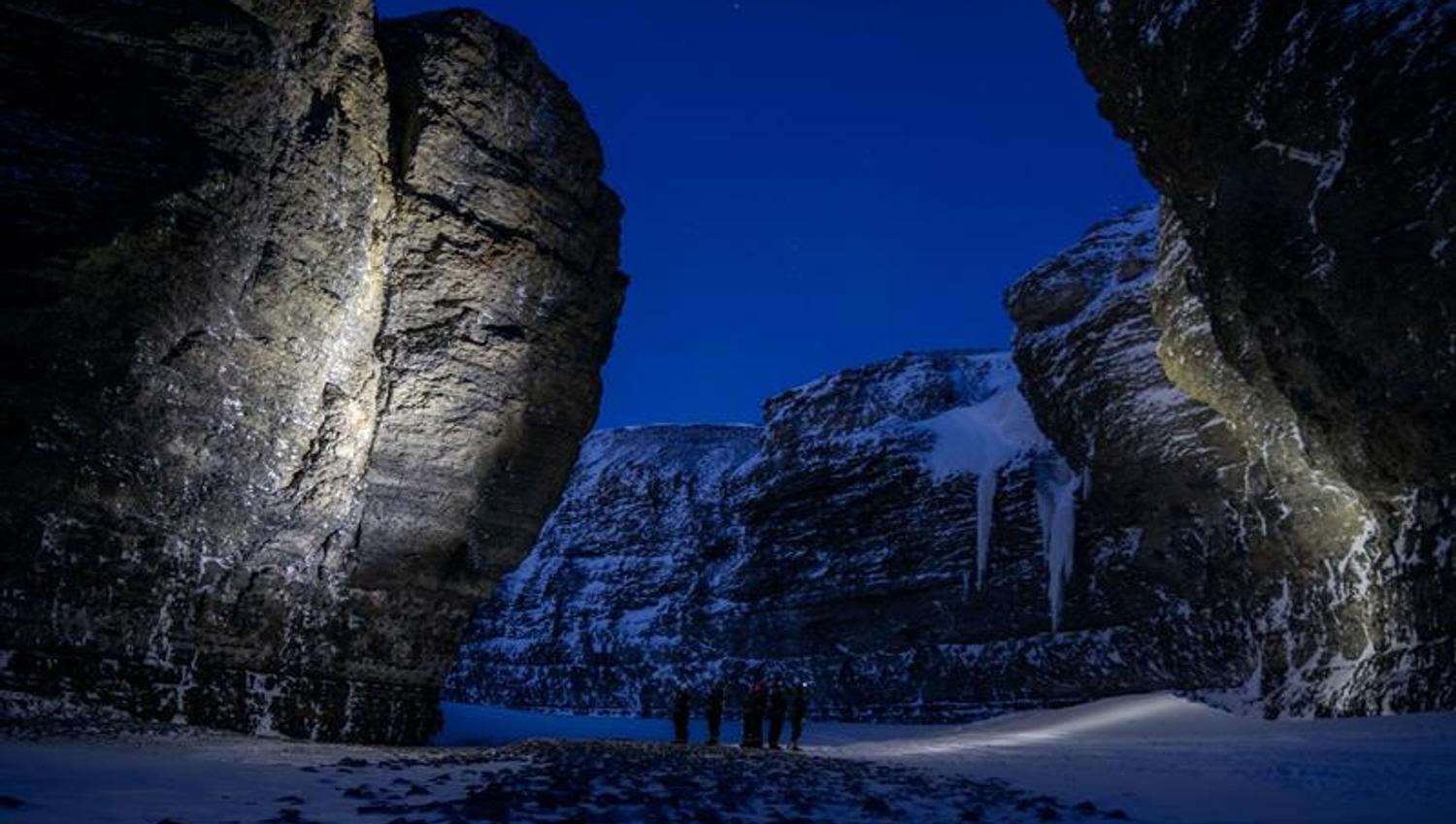 A group of people standing in a valley between mountain cliffs with headplamps on