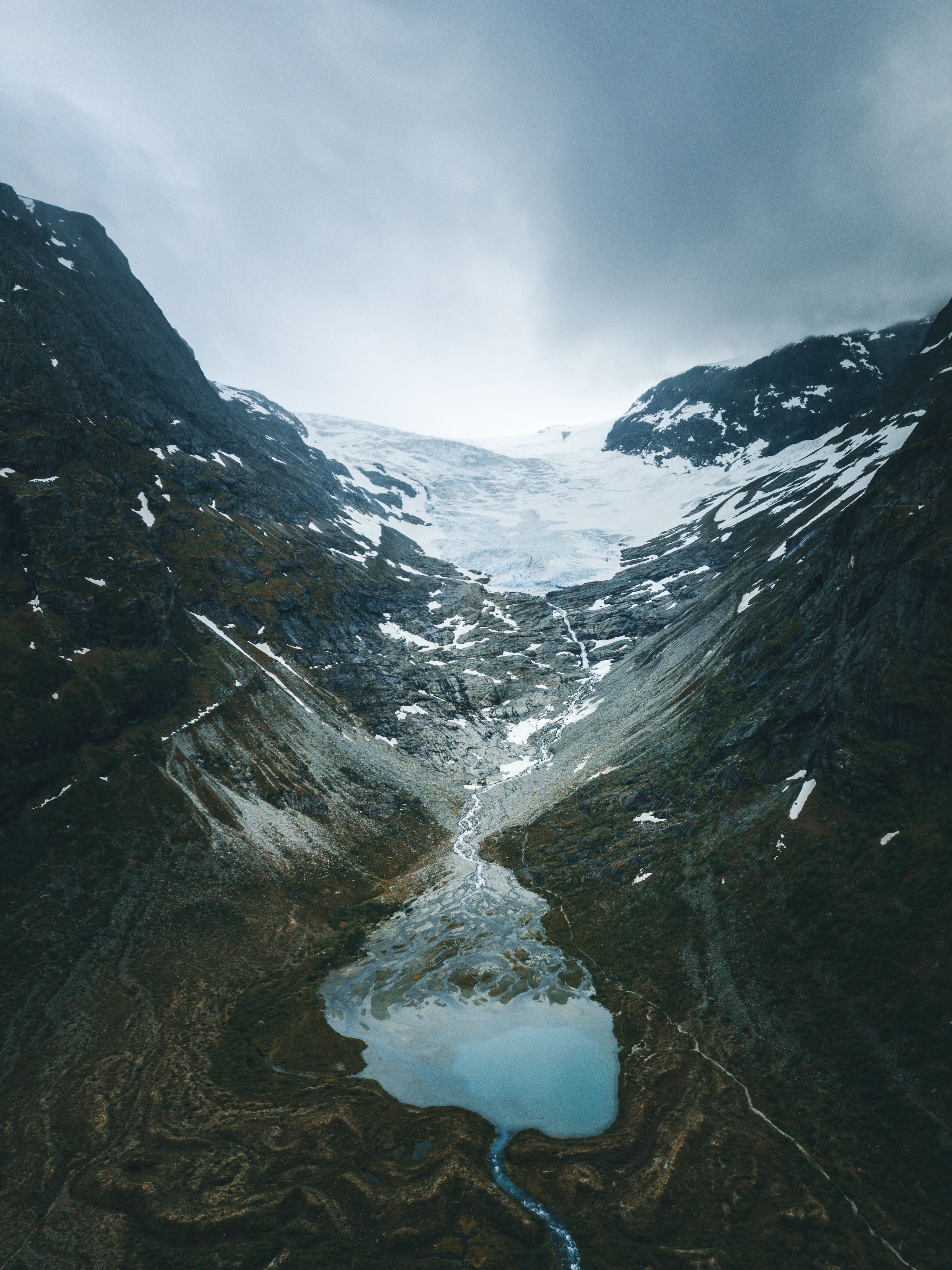 A rugged mountain valley with patches of snow, a glacier at the head, and a pale blue meltwater lake below.