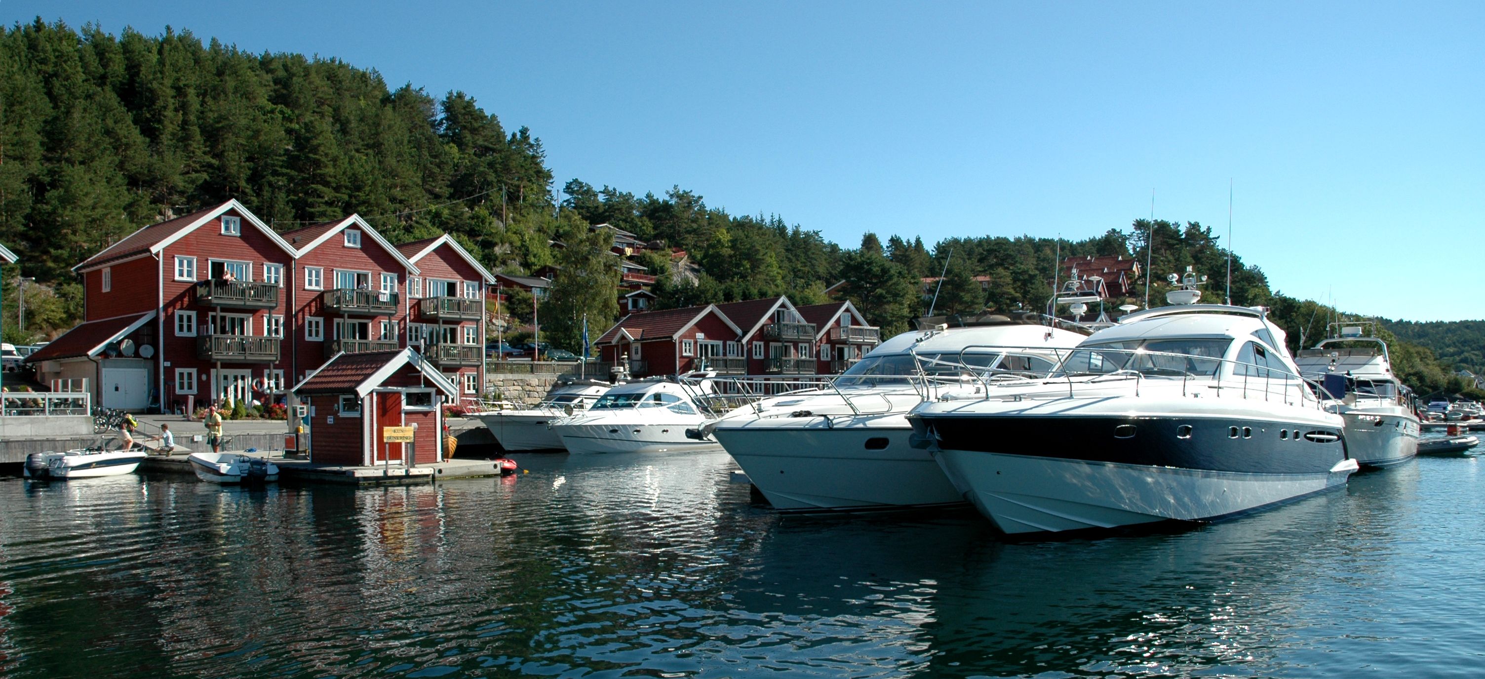 3 store båter står rekke på rad ved brygga, tregde feriehus i bakgrunnen