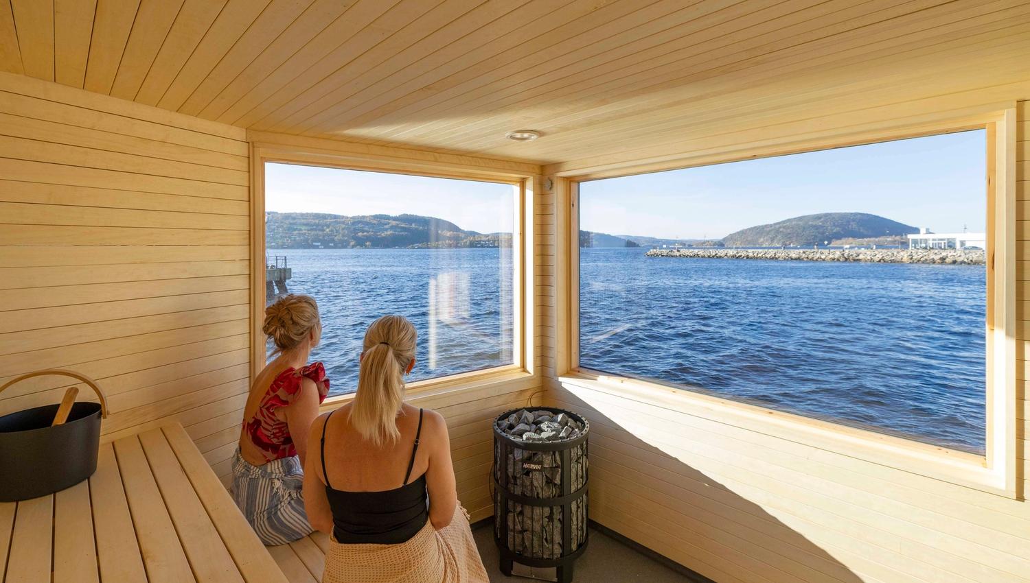 To damer som sitter i badstua med fjordutstikt