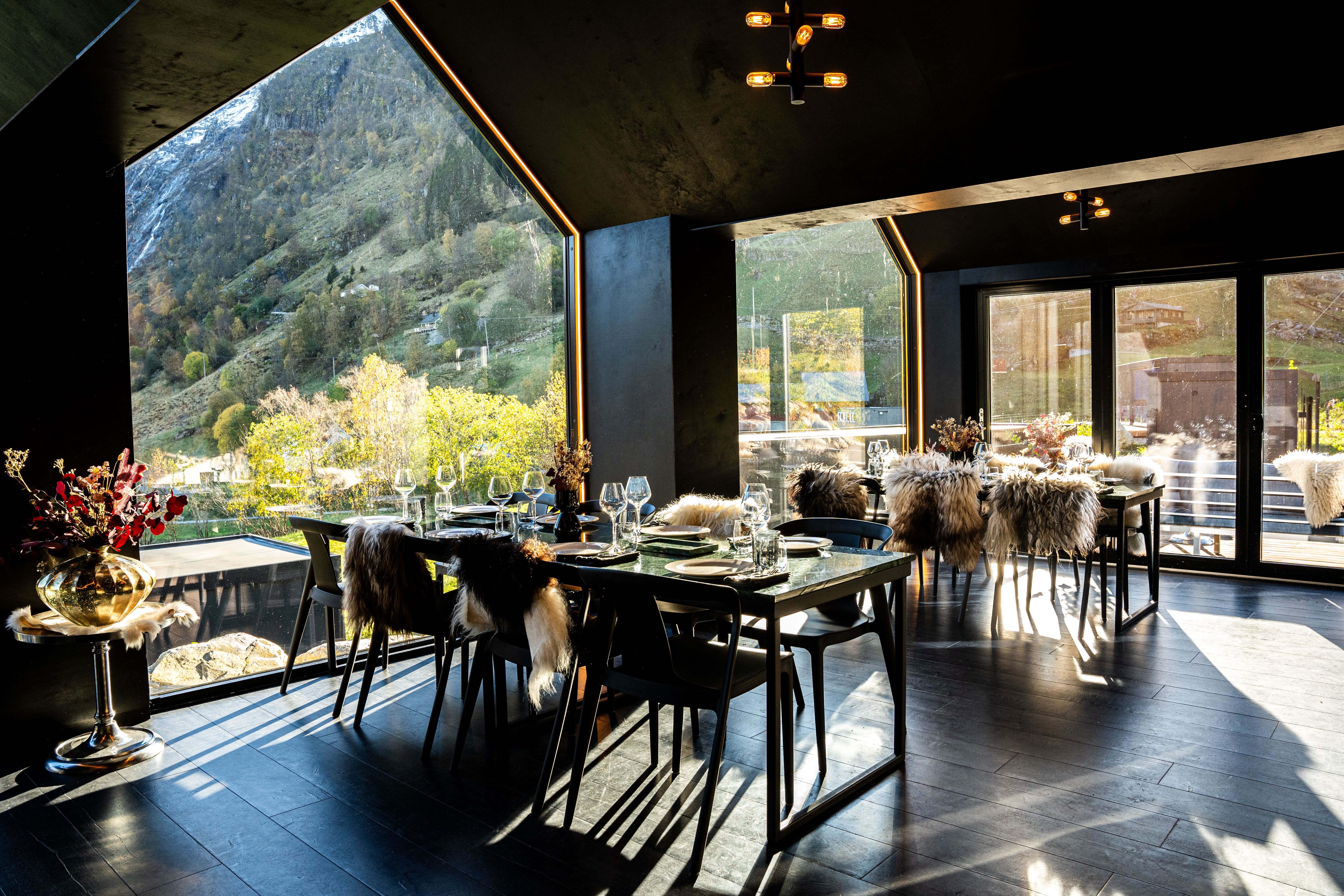 Contemporary dining room with set tables and fur-covered chairs, sunlit through large windows facing mountains at Sølvane Farm Hotel Restaurant in Kandal, Gloppen..