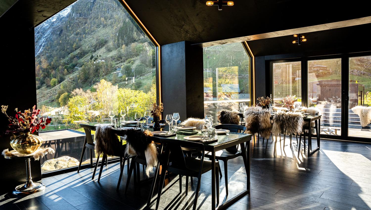 Contemporary dining room with set tables and fur-covered chairs, sunlit through large windows facing mountains at Sølvane Farm Hotel Restaurant in Kandal, Gloppen..