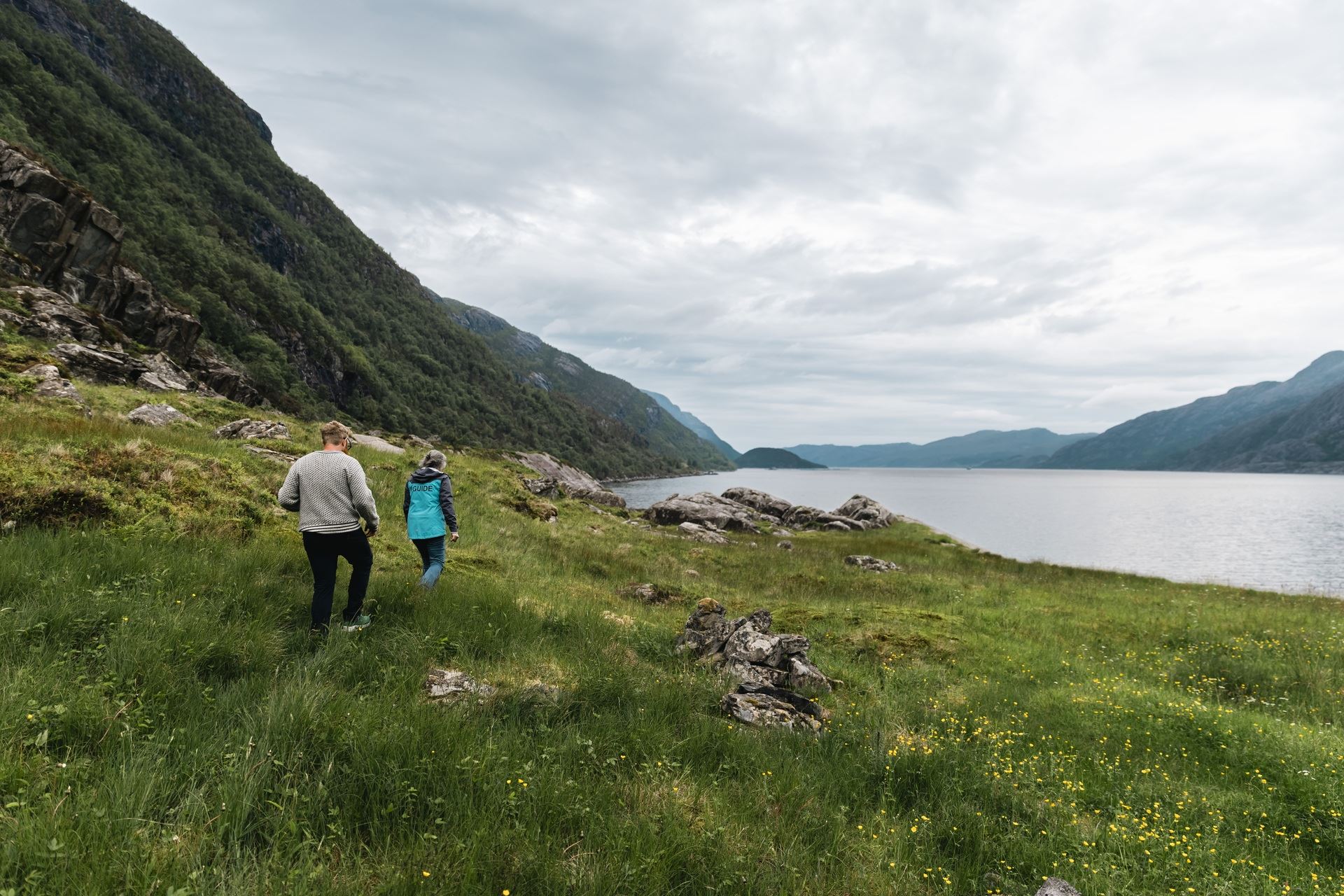 Visitors hiking with guide through the rugged landscape of Vingen, with the fjord and mountains in the background.