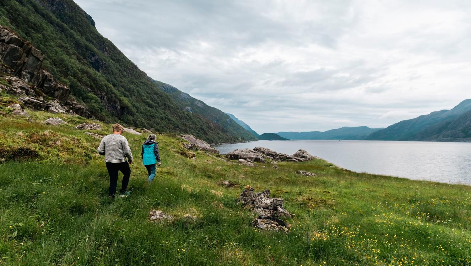 Visitors hiking with guide through the rugged landscape of Vingen, with the fjord and mountains in the background.