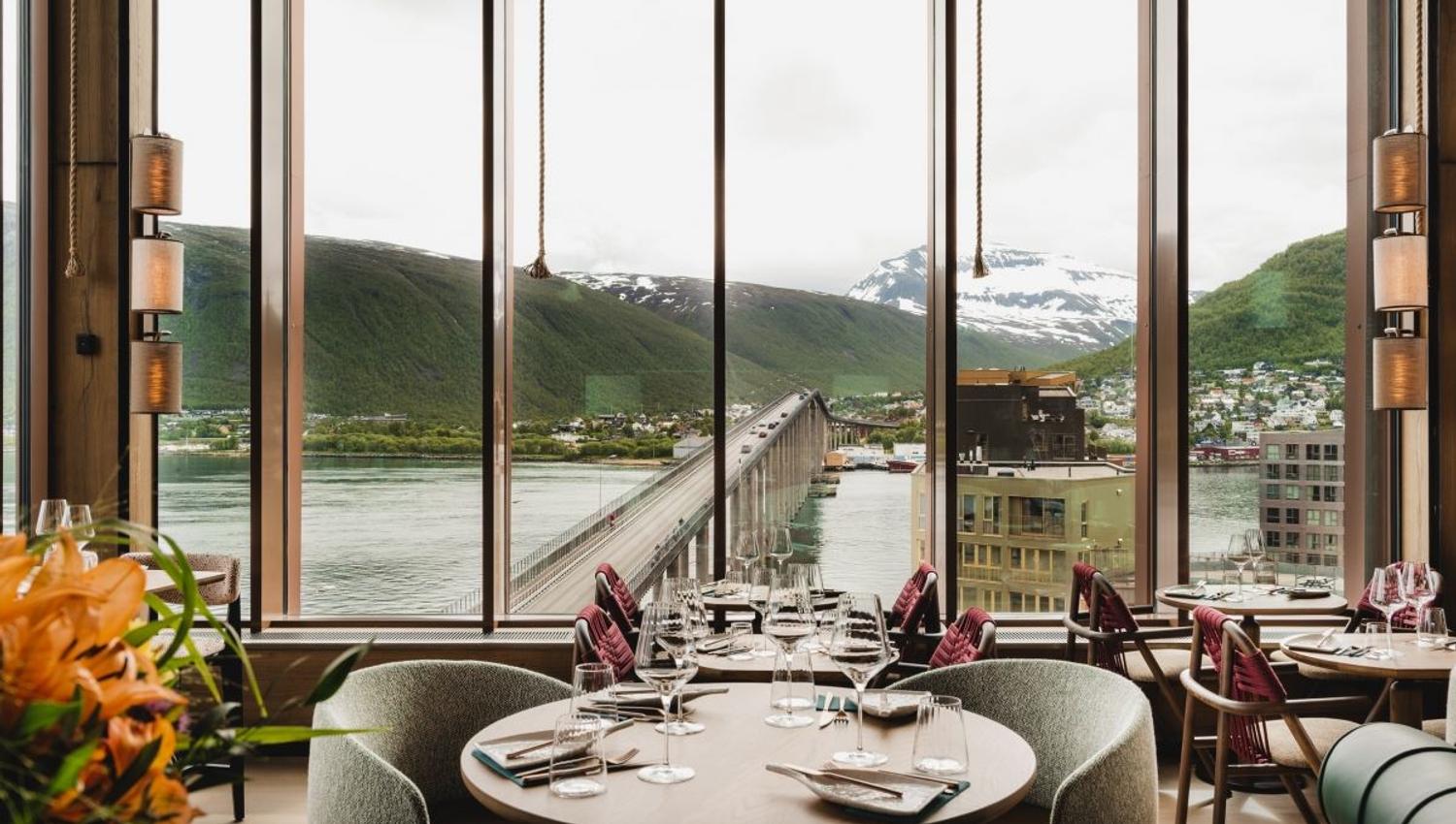 Restaurant med utsikt mot bro, vann og fjell gjennom store vinduer