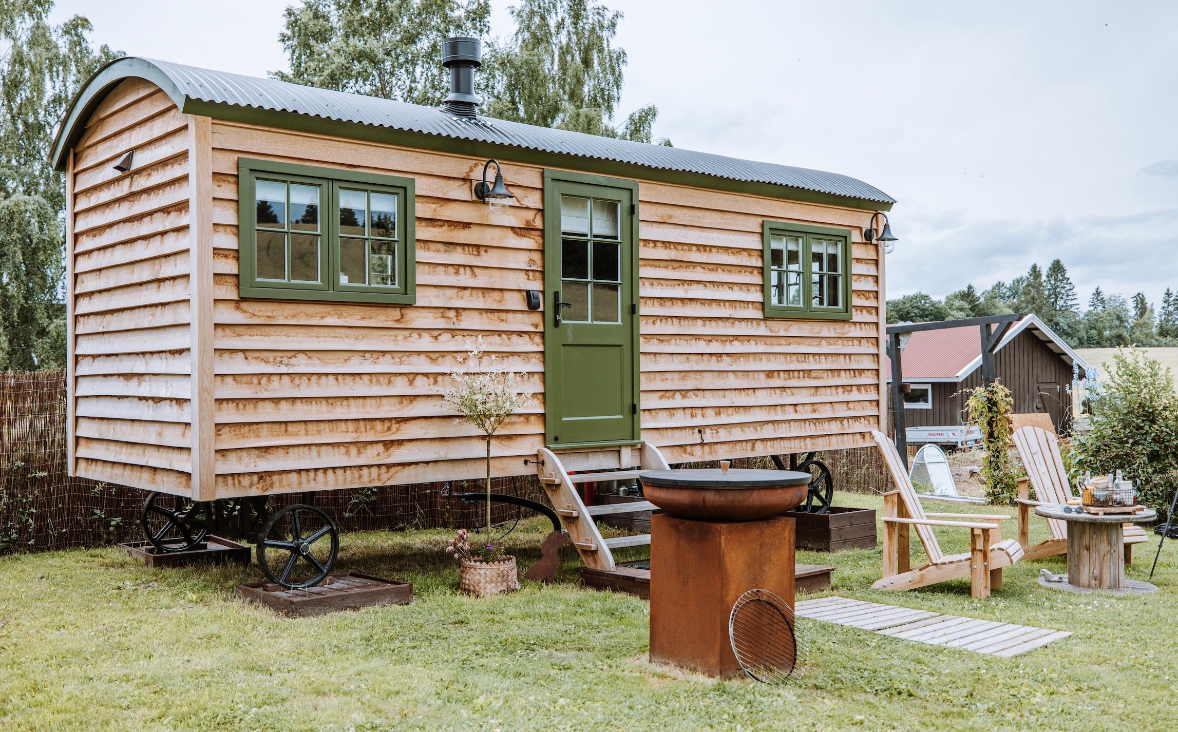 Small wooden house with green windows and chairs in front 
