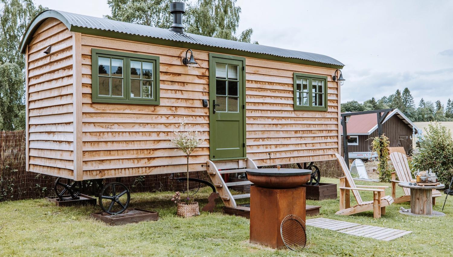 Small wooden house with green windows and chairs in front