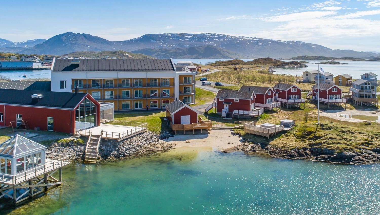 Klart, turkis vann i forgrunnen, med en liten strand og en brygge.