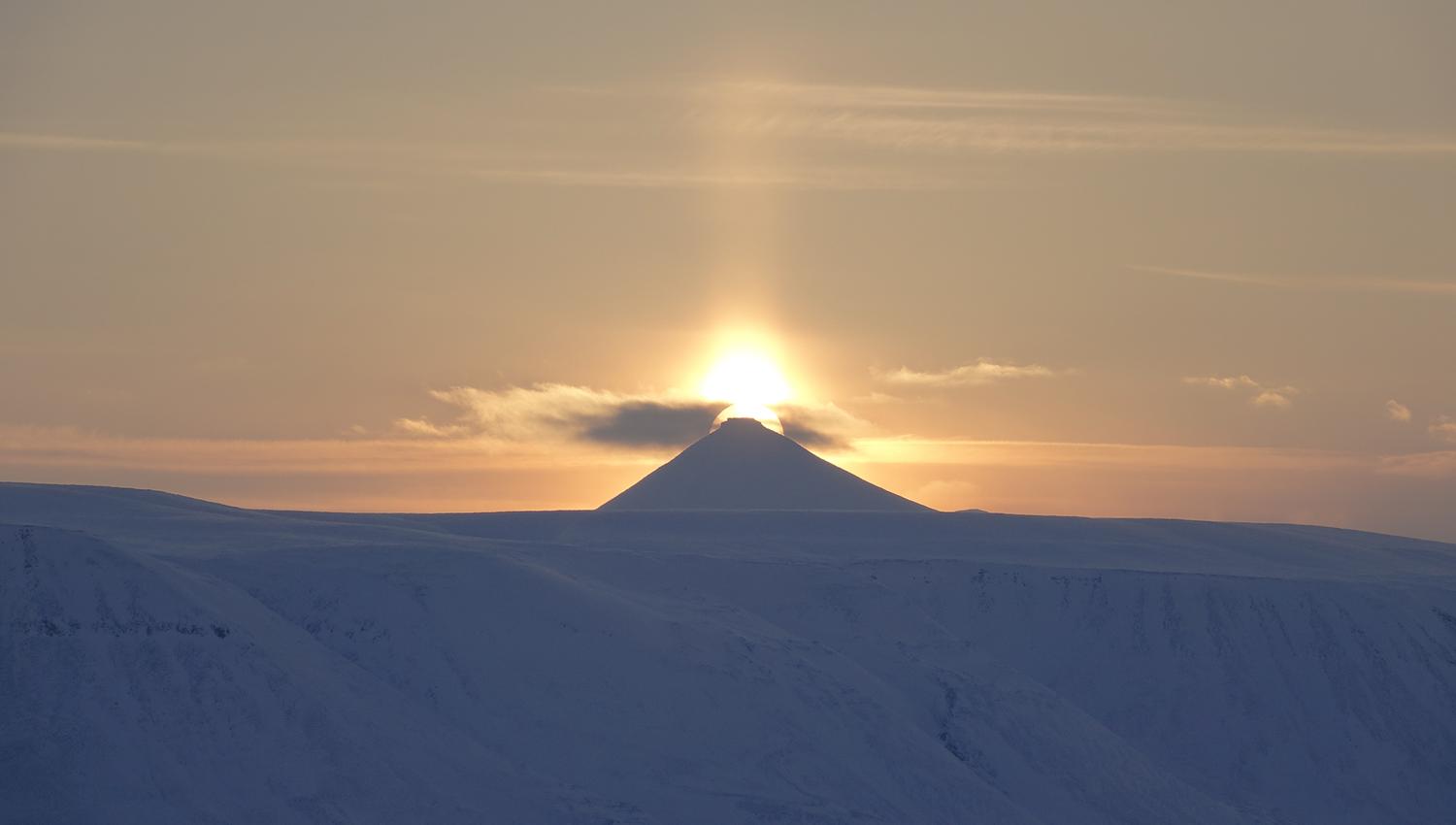 Midnattssola som skinner bak en fjelltopp