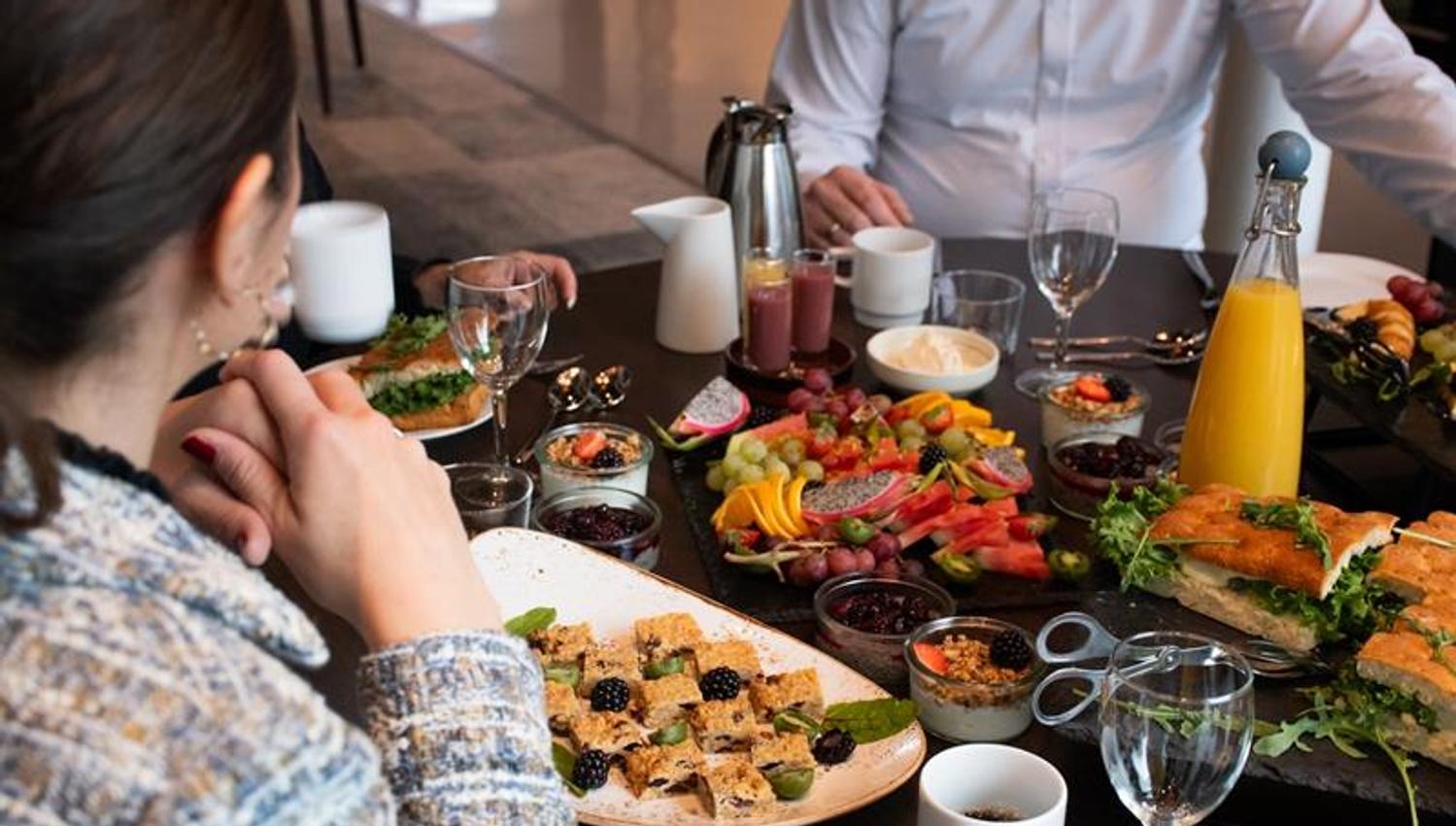 Bord dekket med ulike retter, drikke og kaffe mens flere personer sitter samlet rundt mÄltidet
