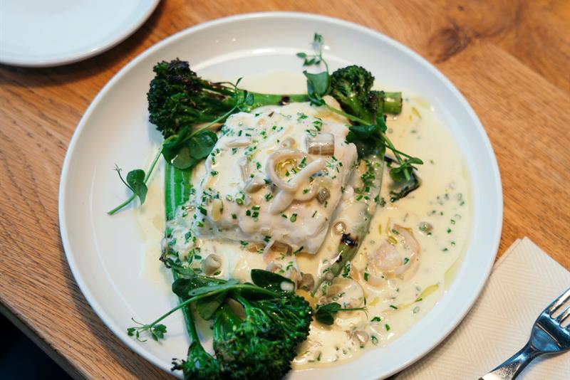 Kremet fiskerett med brokkolini og urter servert i lun atmosfære med levende lys.