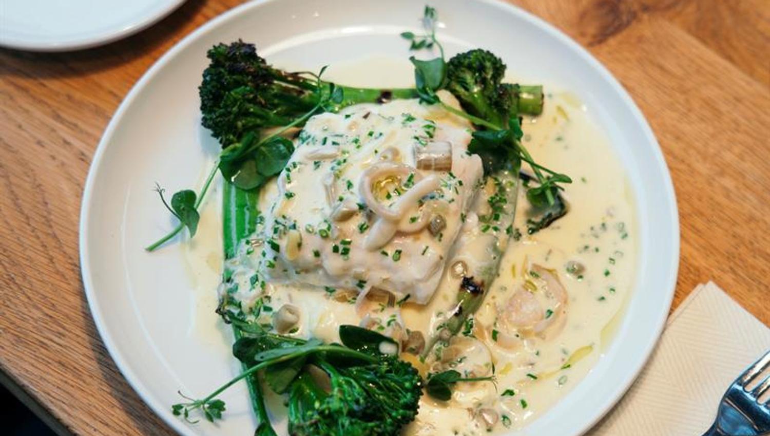 Kremet fiskerett med brokkolini og urter servert i lun atmosfære med levende lys.
