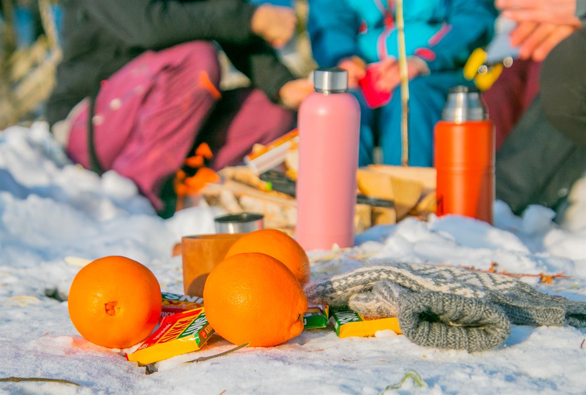Appelsiner, termos og sitteunderlag ligger i snøen under en pause på skitur