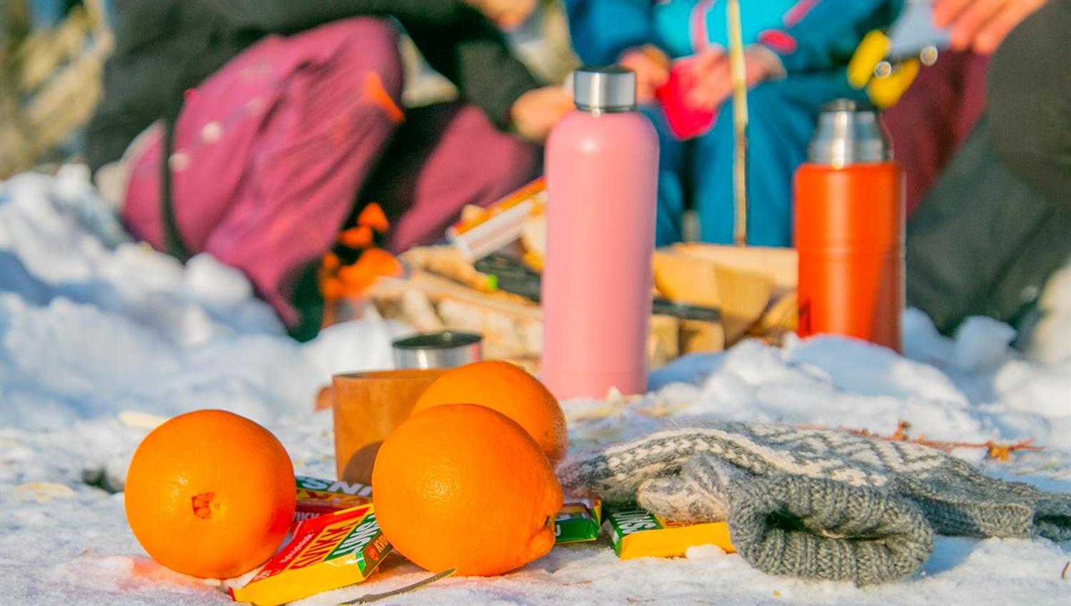 Appelsiner, termos og sitteunderlag ligger i snøen under en pause på skitur