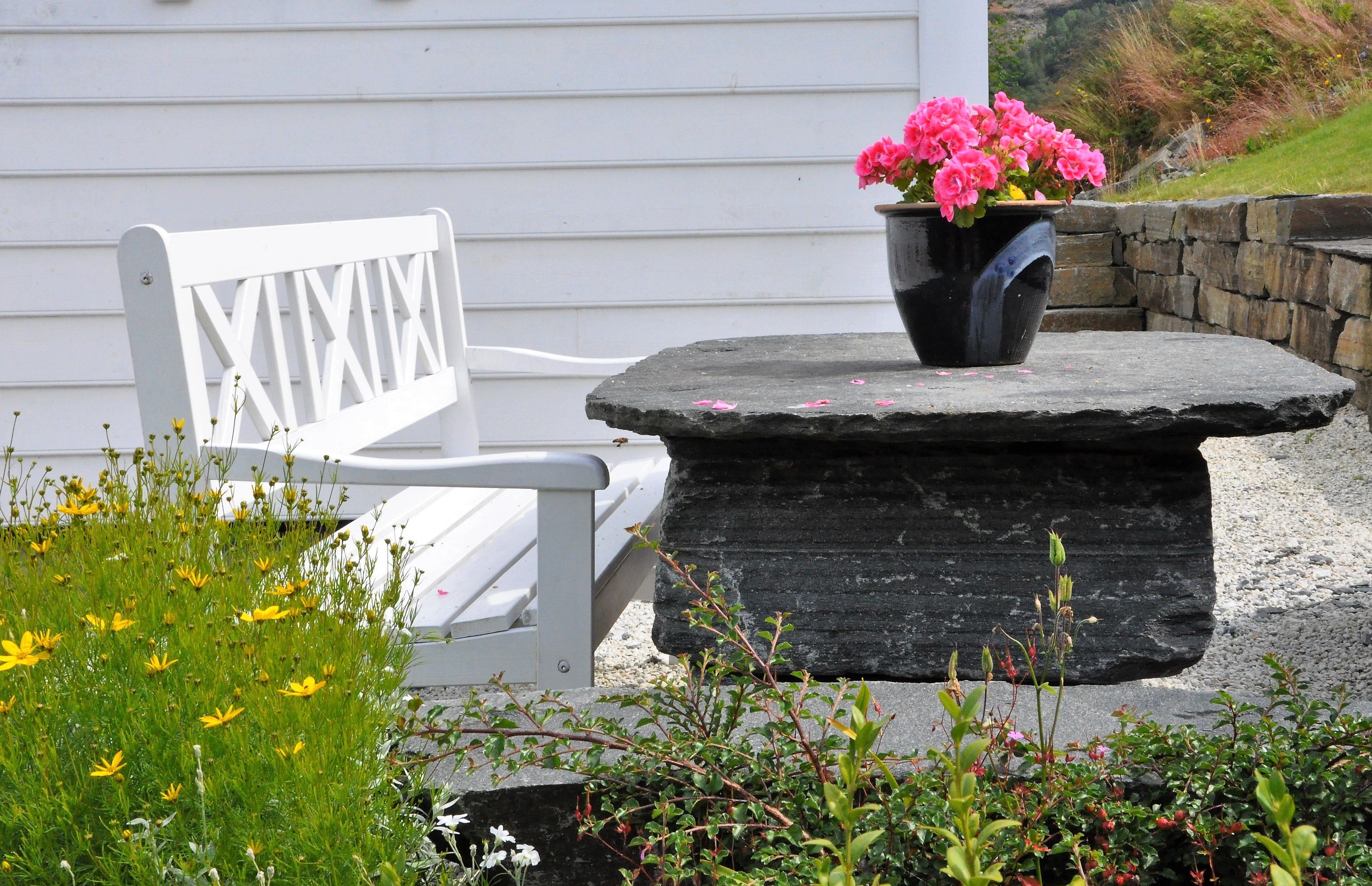 A white bench outside by a stone table with a flower on it. 