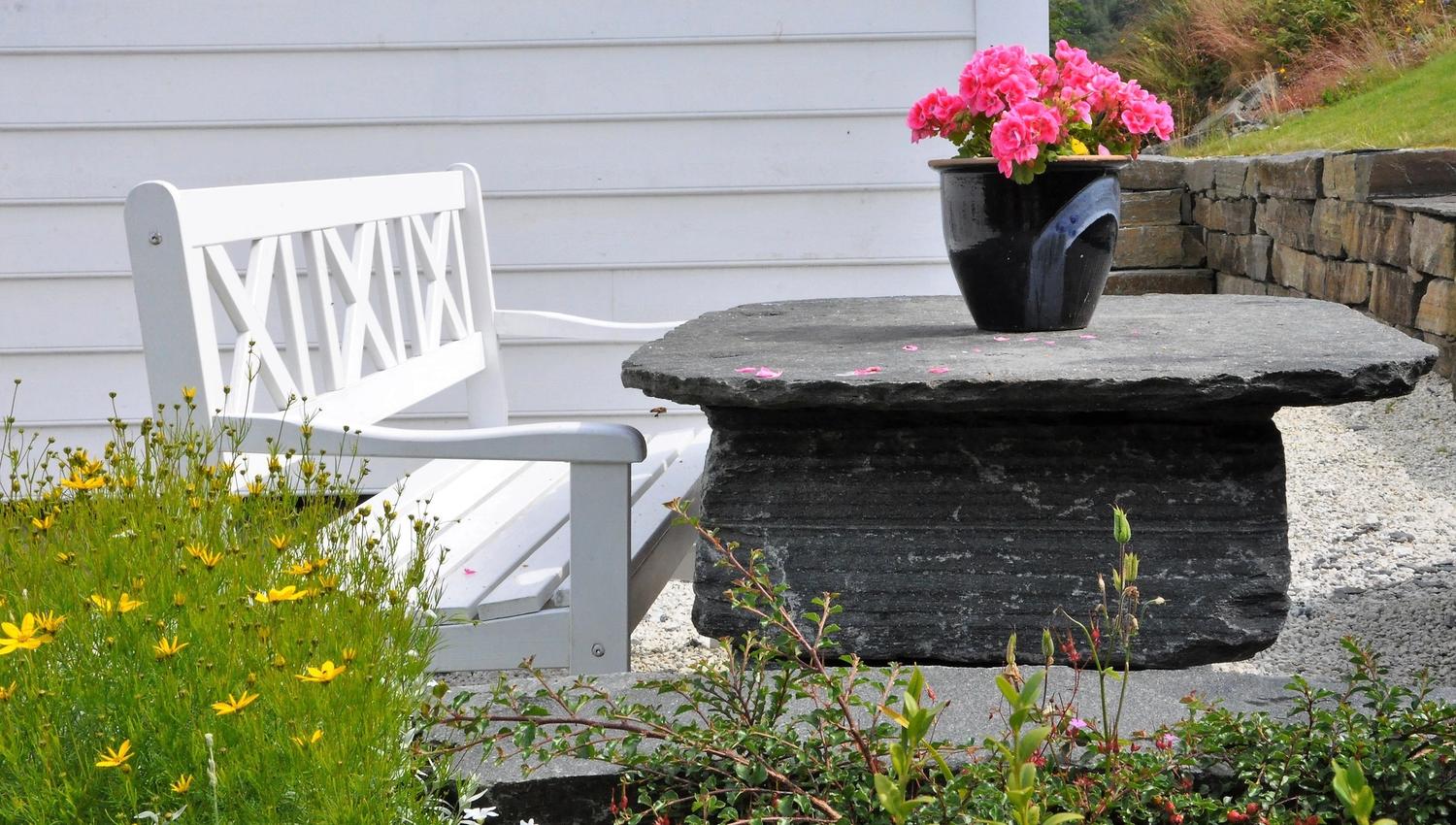 A white bench outside by a stone table with a flower on it.