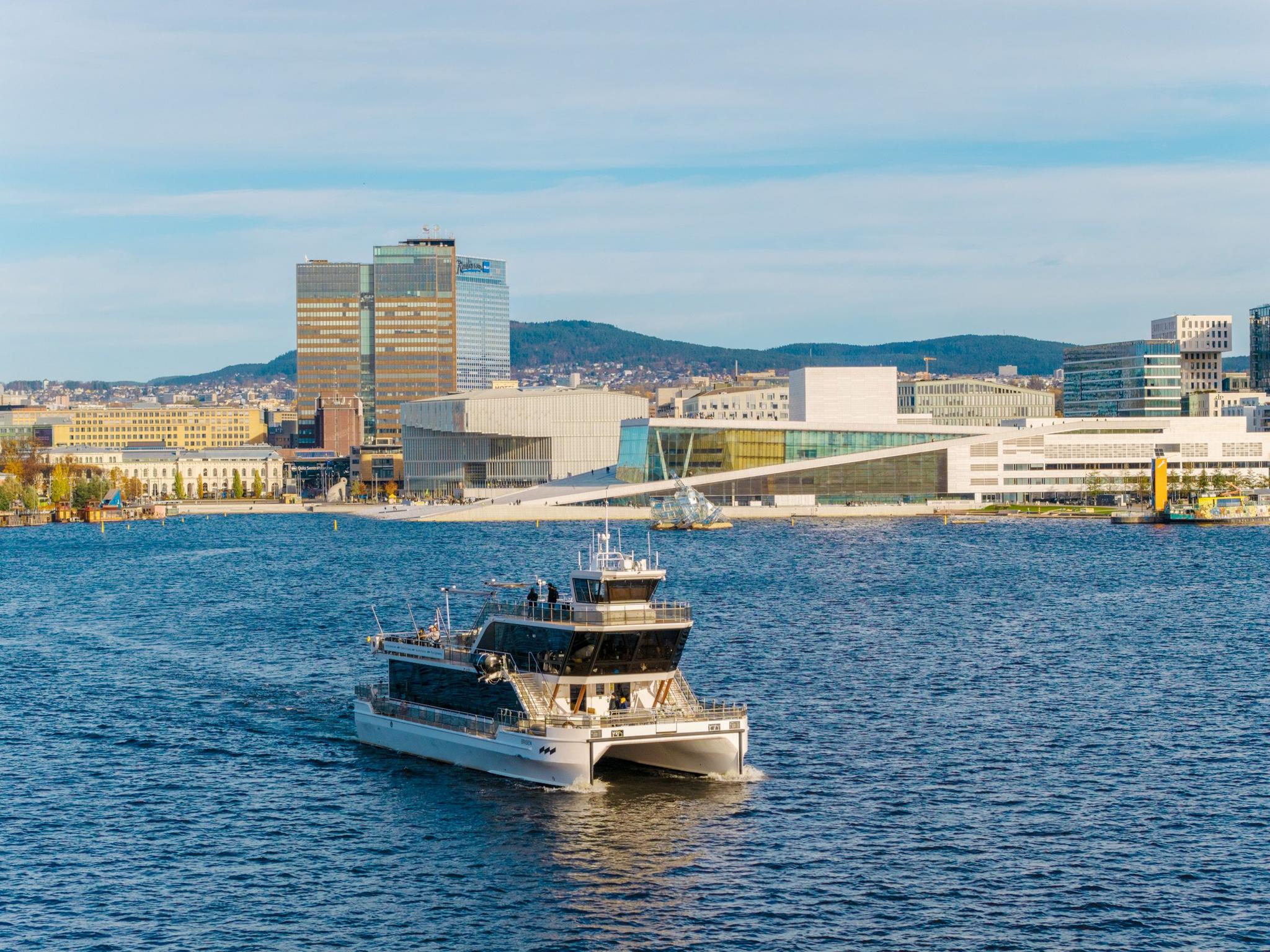 Drone image of the boat in the fjord with the city in the background.