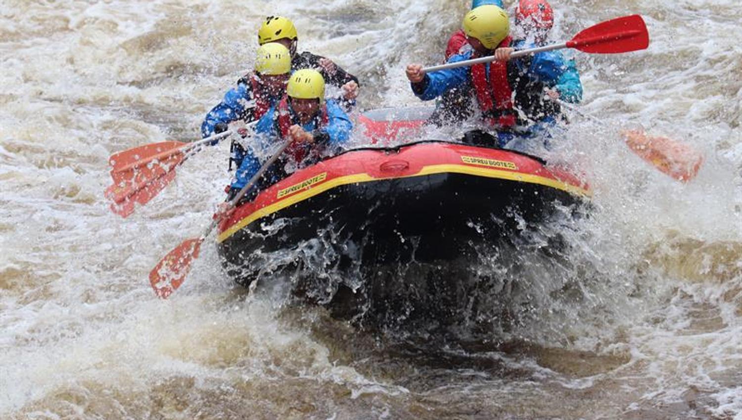 Rafter in einer Welle, viel Wasser spritzt auf das Schlauchboot.