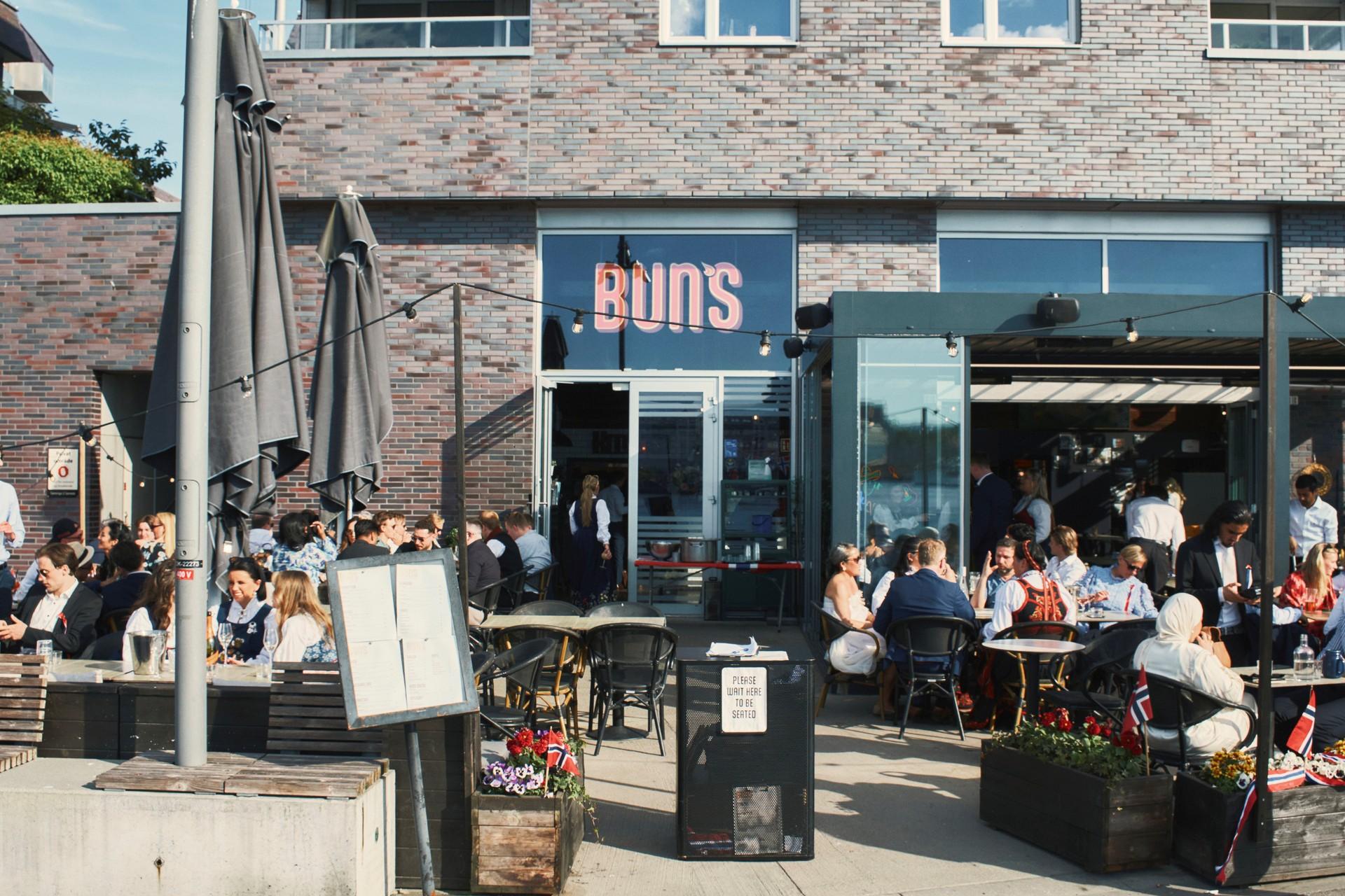 Uteservering med gjester som koser seg i solen foran restauranten.