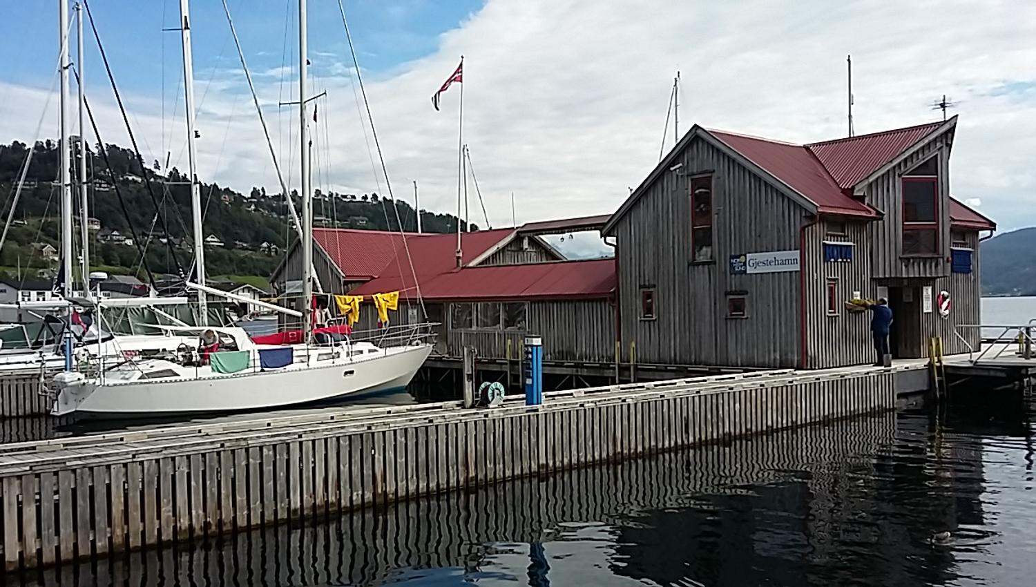 The Norheimsund marina with boats, wooden docks, and maritime buildings with red roofs.