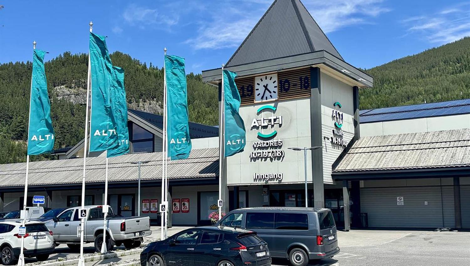 Viser inngangspartiet til Alti med biler foran og alti-flagg som vaier i vinden