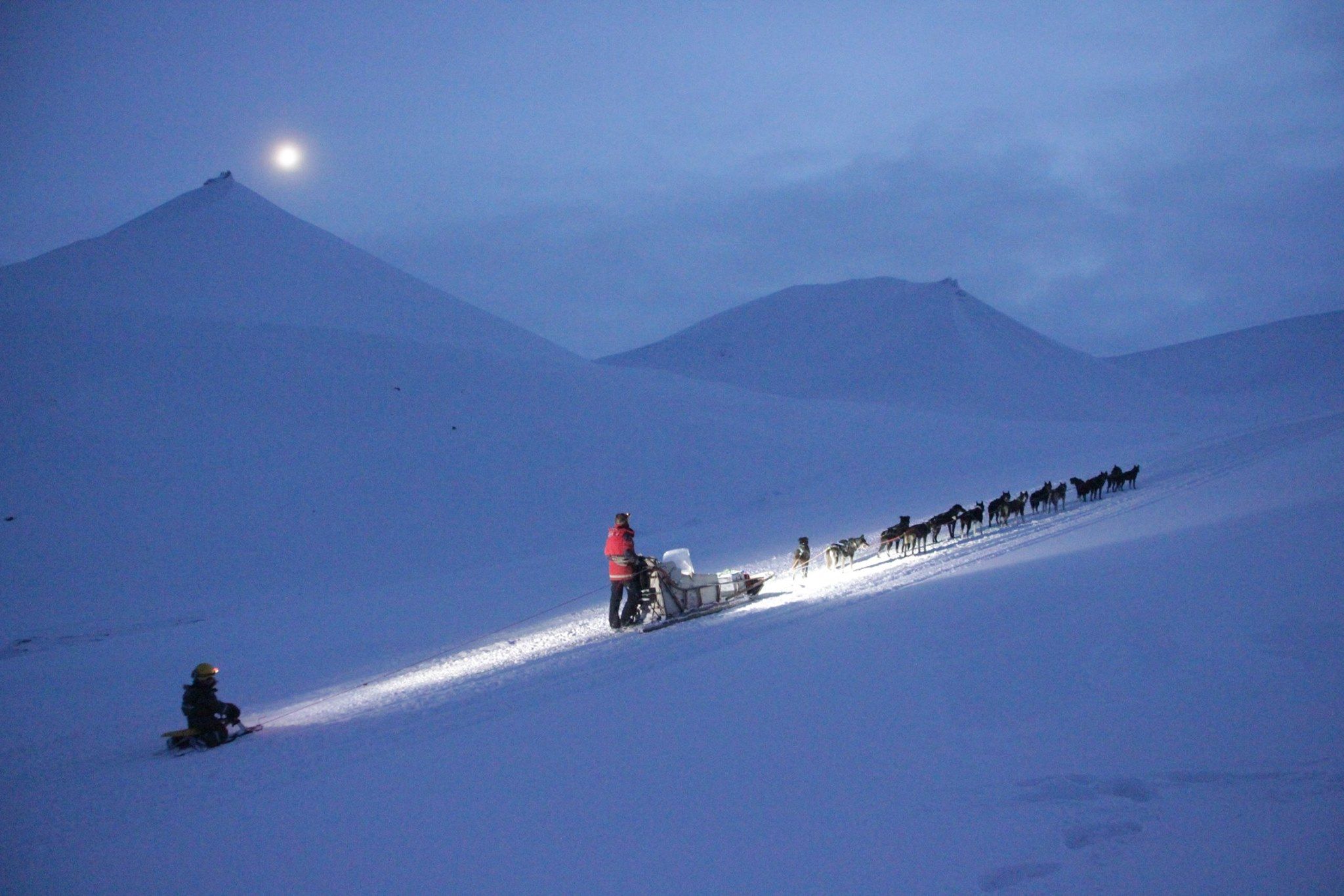 A person driving a dog sled with a child being towed on a children's sled behind