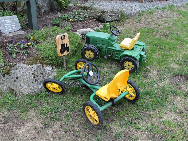 Zwei grüne Spielzeugautos, ein Traktor und ein gokartähnliches Fahrzeug, die am Spielplatz-Parkplatz stehen.