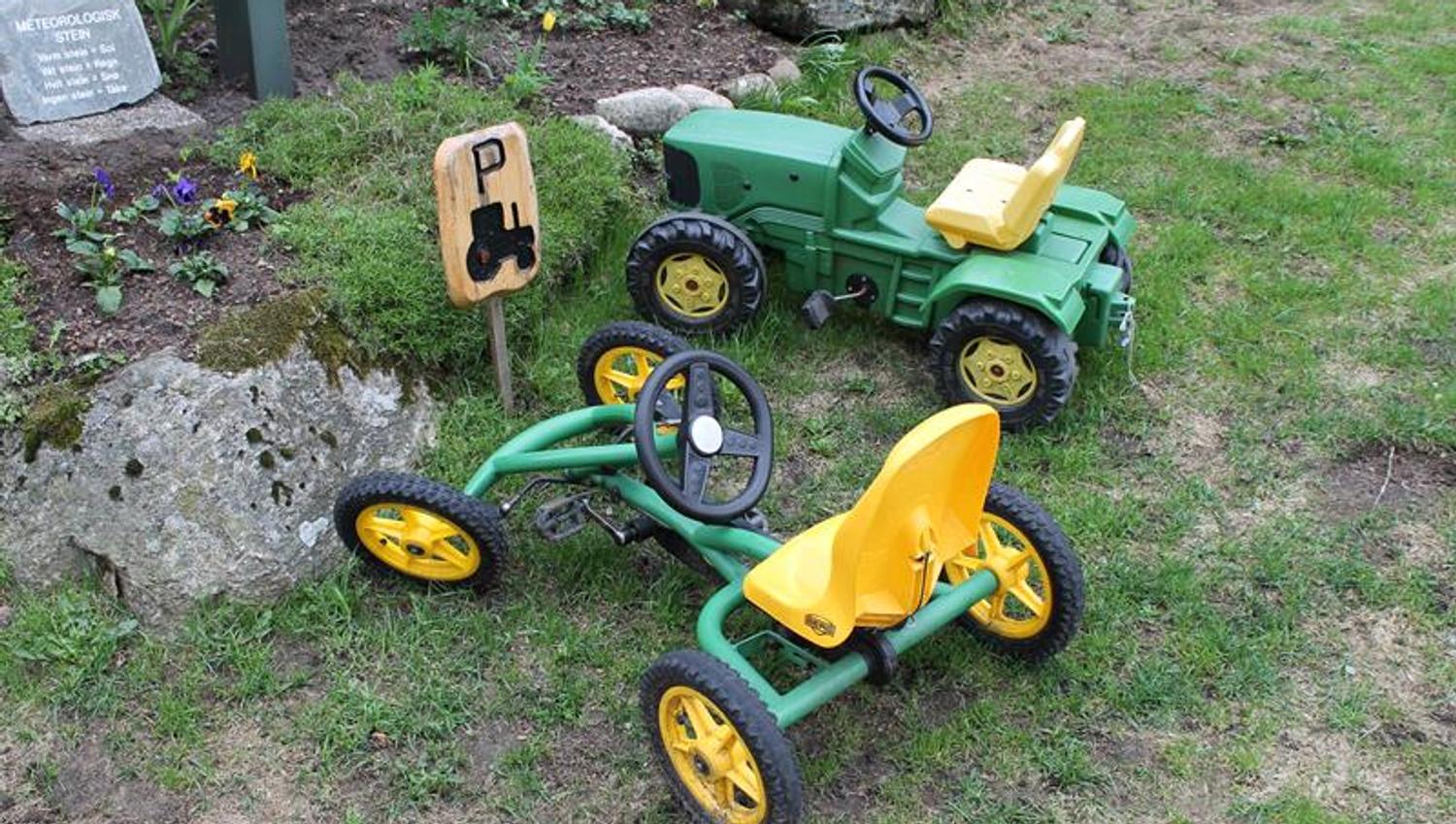 Zwei grüne Spielzeugautos, ein Traktor und ein gokartähnliches Fahrzeug, die am Spielplatz-Parkplatz stehen.