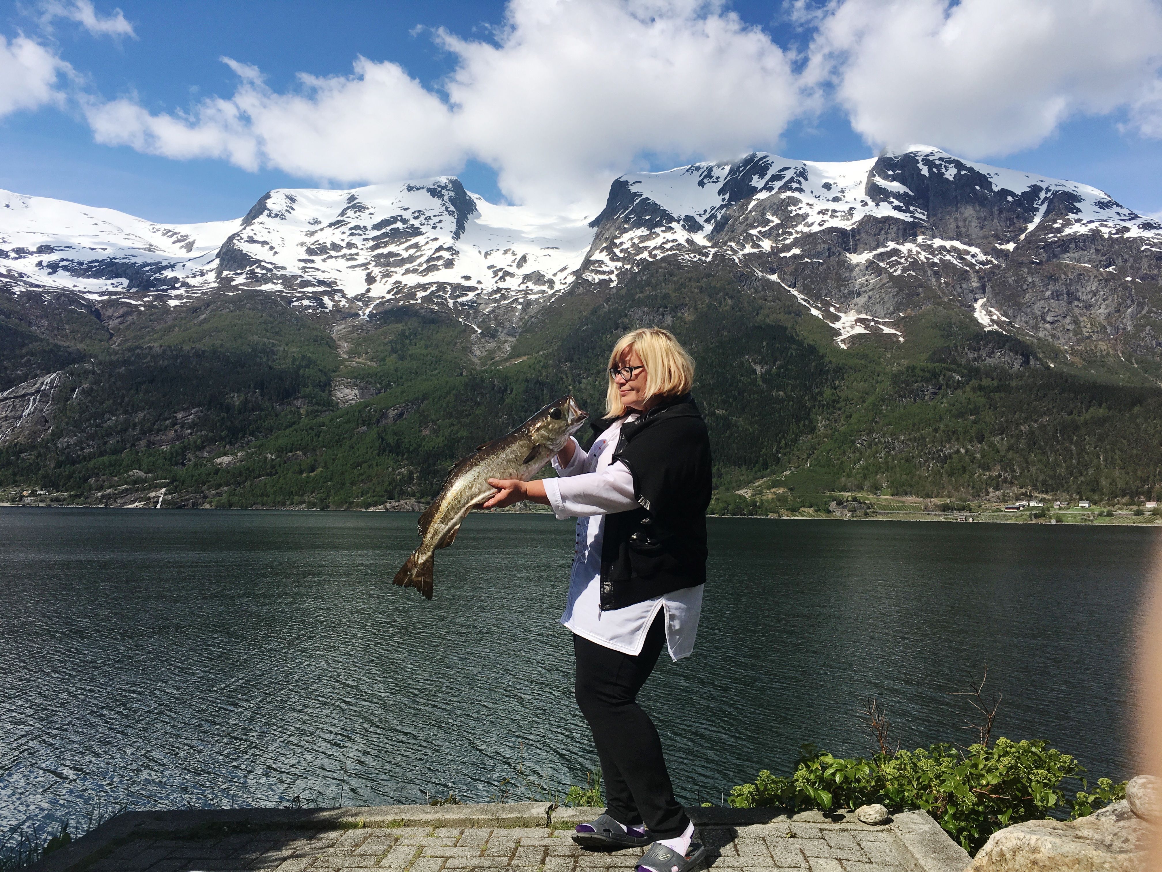 Happy guest proudly holding a large fish by the fjord at Stana Gard – a true fishing experience in the Hardanger region.